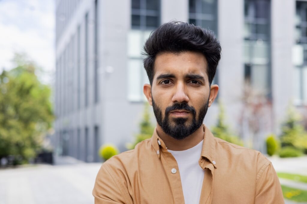 Close-up portrait of young Indian man, serious man concentrating and thoughtfully looking at camera